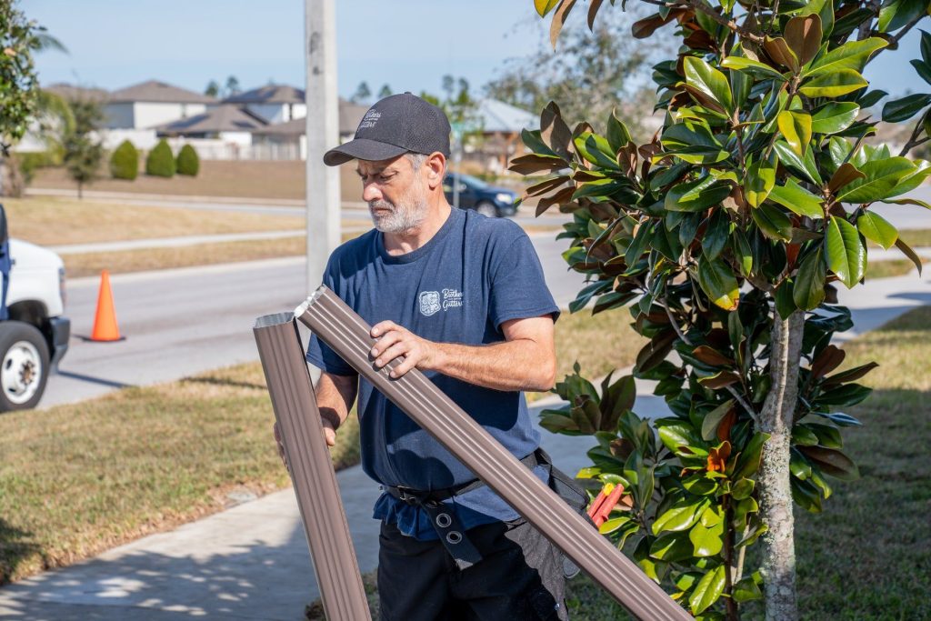 Installer carrying a brown downspout section to the house
