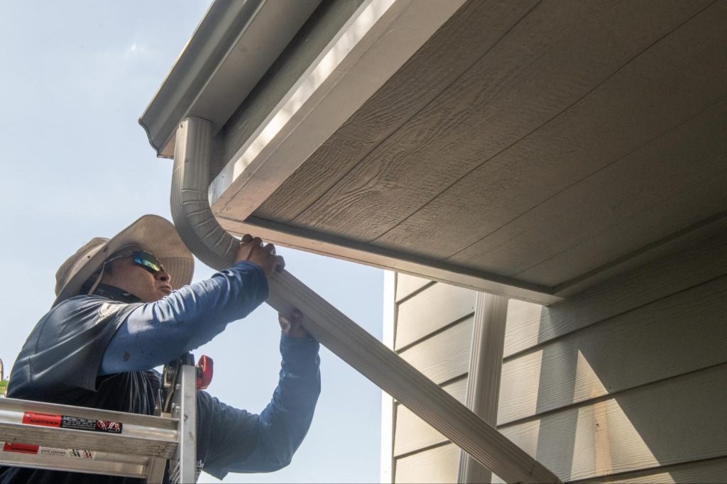 Installer hanging a downspout elbow from the gutter outlet