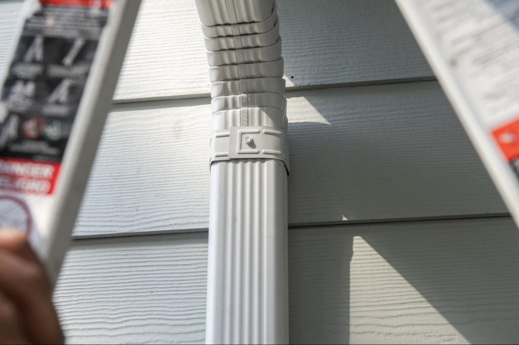 A finished downspout, strapped and sealed against the siding