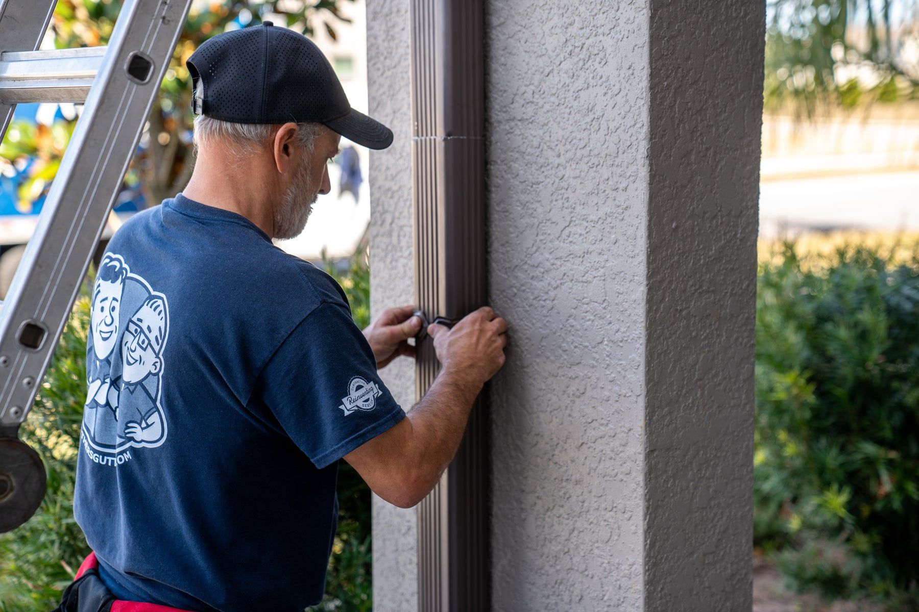 Installer securing a downspout to a stucco wall